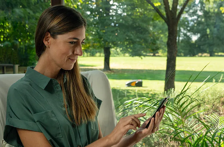 A woman that is controlling her autonomous robot mower through her smartphone